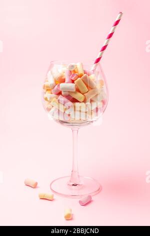 Mini marshmallows in a glass on a light red background. Multi-colored marshmallows in a glass. Confectionery concept. Copy space close-up Stock Photo