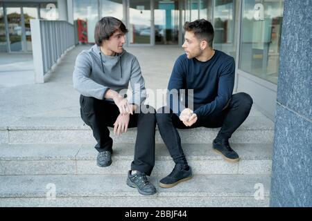 Front view of two young men talking sitting on a city staircase and Stock Photo