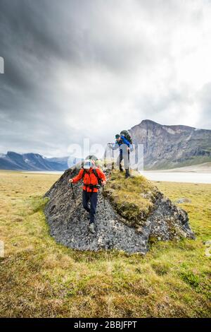 Backpackers hiking over large boulder in Akshayak Pass. Stock Photo