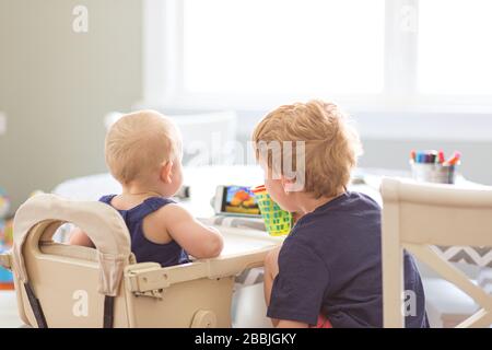 back view baby girl and young brother looking at phone at table indoor Stock Photo