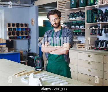 Smiling woodworker. Cheerful young male carpenter leaning at the wooden table with diverse working tools laying on it Stock Photo