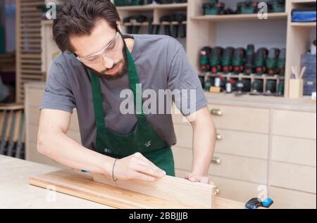 profession, carpentry, woodwork and people concept - carpenter testing wood plank evenness at workshop Stock Photo
