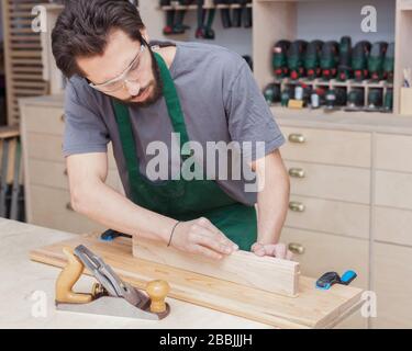 profession, carpentry, woodwork and people concept - carpenter testing wood plank evenness at workshop Stock Photo