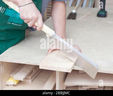 The carpenter's hands. Young bearded hipster in a carpentry workshop saws cool Japanese saw. Stock Photo