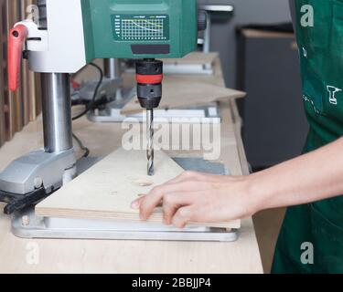 Close up. Carpenter at work using vertical drilling machine. Workshop. Stock Photo