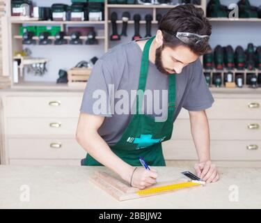 Young carpenter or woodworker with safety glasses, work apron, and ...