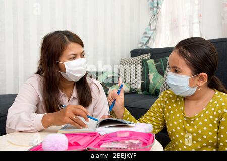 Home schooling concept image with mother and daughter studying while wearing face masks because of current corona virus threat - Current health care / Stock Photo
