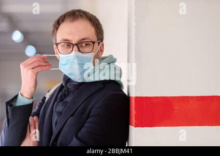 Sick European man in glasses wearing protective medical mask, standing near the wall with red line. Flu epidemic, dust and pollen allergy, protection Stock Photo