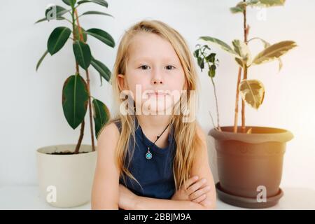 Little boy standing with arms-crossed. Pottet plants on the table behind Stock Photo