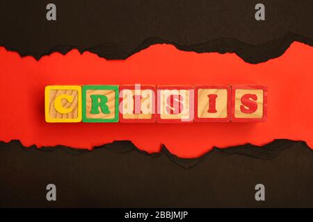 Word CRISIS made from wooden letters lies on a red and black background.