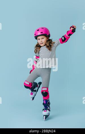 Focused little girl trying to hold balance in roller skates over blue Stock Photo