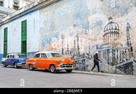 Old American Cars and wall mural of Havana, Cuba Stock Photo