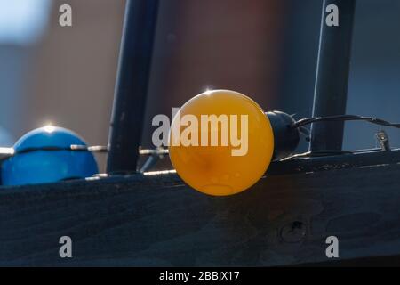 a close up view of a bright orange coloured light bulb connected to a row of differnat colours on the top of a fence Stock Photo