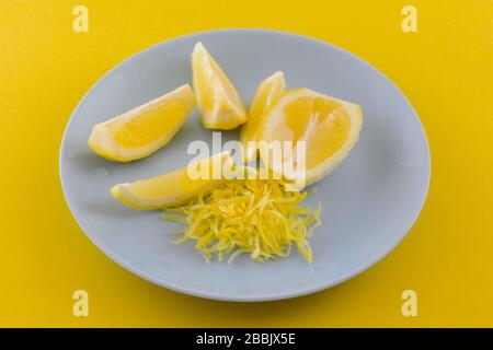 Lemon half, lemon wedges and lemon zest on blue plate on yellow background Stock Photo