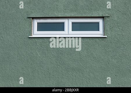 a close up view of two small white windows with a rough green painted wall Stock Photo