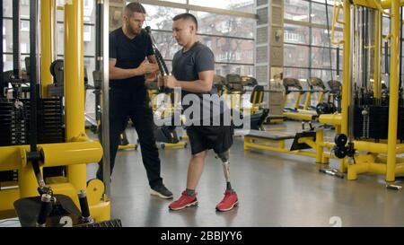 Disabled young man with instructor working out in gym Stock Photo
