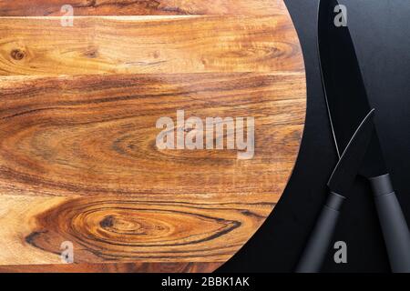 Wooden chopping board and black knifes on black background. Stock Photo