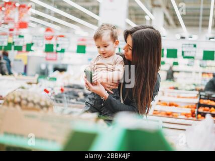 Young woman mother with cute baby boy toddler child on hands buys the freshavocado in supermarket Stock Photo