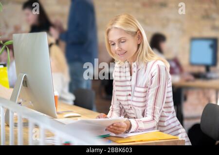 Blonde woman sitting at desk, checking notes Stock Photo