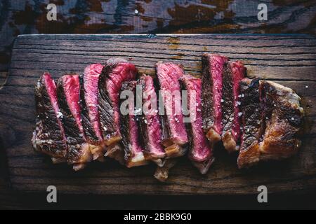 Delicious homemade medium rare black Angus sliced steak with sea salt on a wooden board top view American food Stock Photo