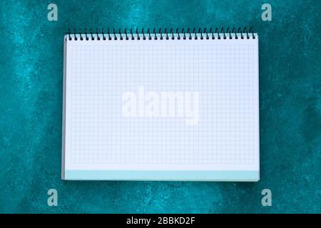 Empty squared notebook with copy space for text on abstract green painted background. Planning concept. White paper sheet, mock-up Stock Photo