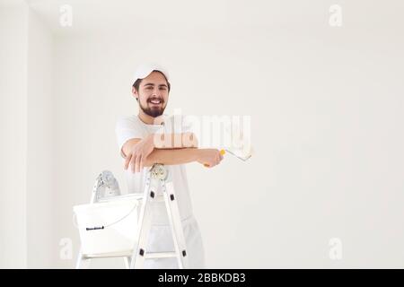 A male painter in a white uniform with a roller works in his hand in a white room Stock Photo