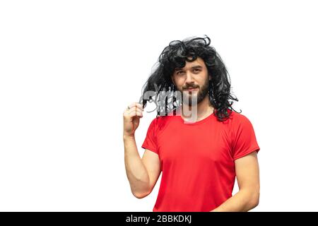 Handsome smiling bearded man in wig of curly long messy hair and red t-shirt isolated on white. Copy space. Exotic hair-do. Time to visit barbershop. Stock Photo