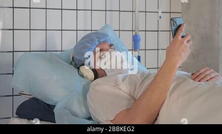Young male patient lying in a bed in hospital and listening to music using headphones. Stock Photo
