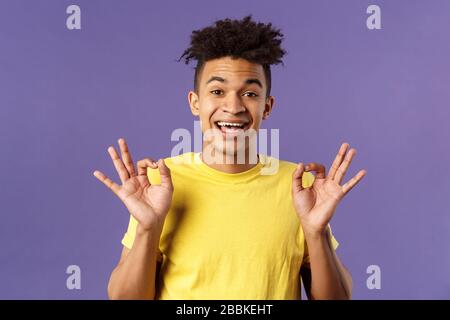 Close-up portrait of upbeat, relaxed young hipster guy with dreads assuring all good, everything be okay, show OK gesture and smiling, no problem Stock Photo