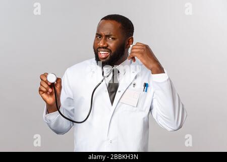 Covid19, hospital check-up and healthcare concept. Portrait of confused grimacing african-american doctor cant hear anything as patient talking during Stock Photo