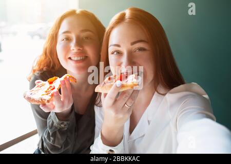 Female models take a selfie on a phone in caffee. Young women smiling and eating pizza Stock Photo