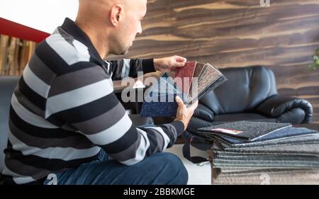 Man choosing the right colour and material of carpet for his new apartment in floor studio, furnishing households Stock Photo