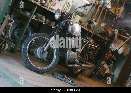 Old motorcycle, which needs to be repaired, in the workshop, with set of tools Stock Photo