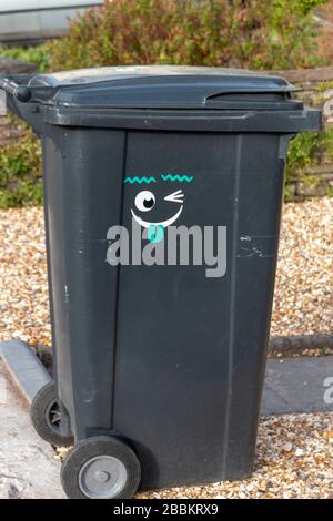a close up view of a black wheeling rubbish bin with a funny face sticker on the side Stock Photo