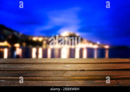 Wooden table with blue blue sky and illuminated city near sea background, beautiful harbor during evening time. Background Image of wooden table Stock Photo