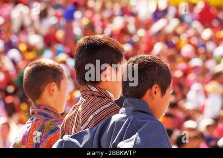 Three young boys in traditional national costume watching the celebrations at the Thimphu Tsechu Festival, Rear view portrait, head and shoulders only. Stock Photo