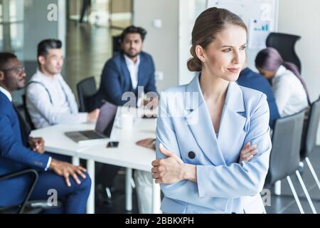Business woman stands on the background of partners. A team of young businessmen working and communicating together in an office. Corporate Stock Photo