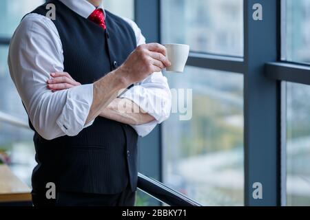 Smiling happy managing director thinks about his successful career development while standing with a cup of coffee in his hand in his office near the Stock Photo