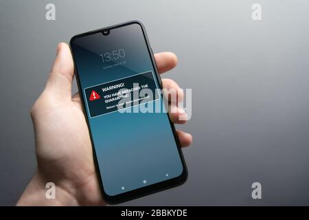 Quarantine breach alert mockup on smartphone being held in hand. Advice to stay in home quarantine to stop contagion. Pandemic, healthcare, technology Stock Photo