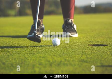 Pretty young woman playing golf on training ground, hits the golf ball into the hole, sport concept Stock Photo