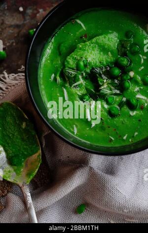 Green peas and spinach puree soup in a black bowl. Vegetarian cream soup on gray background. Healthy eating during quarantine. Stock Photo