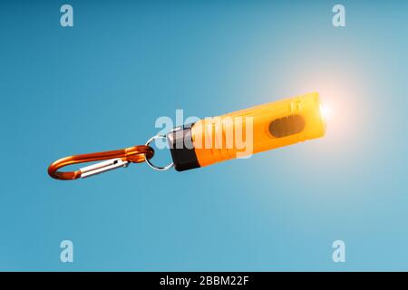 An orange led flashlight with a carabiner glows on a blue background. Stock Photo