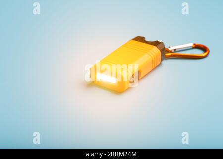 Orange led Flashlight with a carabiner on a blue background. LED lights in flight. Stock Photo