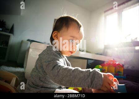 Portrait of one year old baby girl indoors in bright room playing by herself Stock Photo