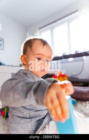 Portrait of one year old baby girl indoors in bright room playing by herself