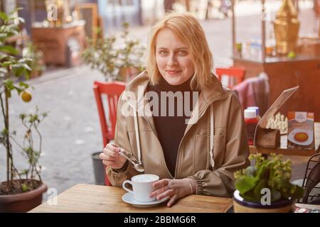 Smiling young caucasian woman is relaxing in a street cafe in Istanbul with a cup of coffee. White female tourist travels to Turkey. Stock Photo