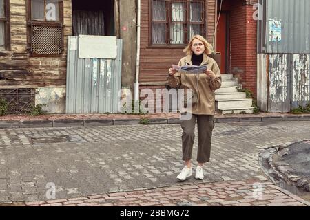 A young Caucasian woman, dressed in warm winter clothes, walks along the deserted streets of Istanbul with a paper map during a tourist trip to Turkey Stock Photo
