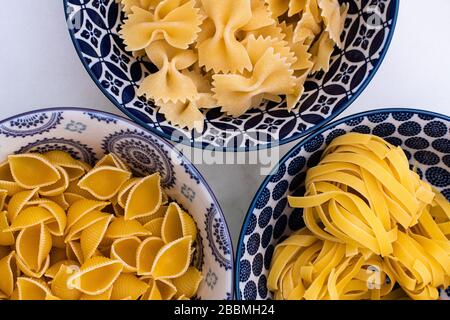 Different dry pasta shapes in patterned bowls on a white marble worktop Stock Photo