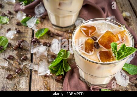 Cold summer coffee, latte, frappe, frappuccino. Coffee iced cocktail drink with frozen coffee ice cubes, milk or non-dairy milk and mint leaves. Woode