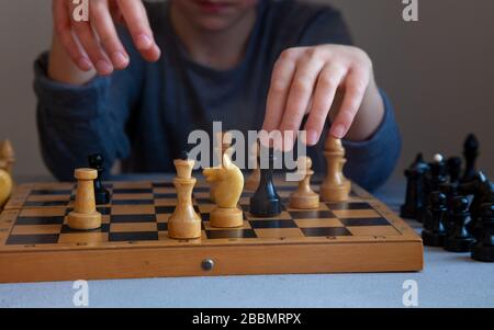 A child plays chess alone. Old wooden chessboard. Children's hands. Chess pieces on a chessboard. Stock Photo